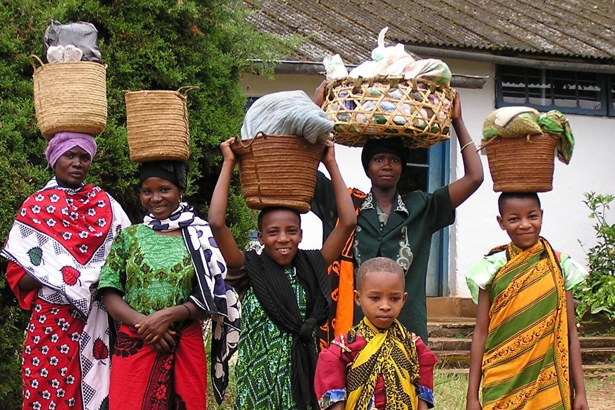 Tansanialaisia naisia värikkäissä asuissa kantamassa tavaroita koreissa pään päällä